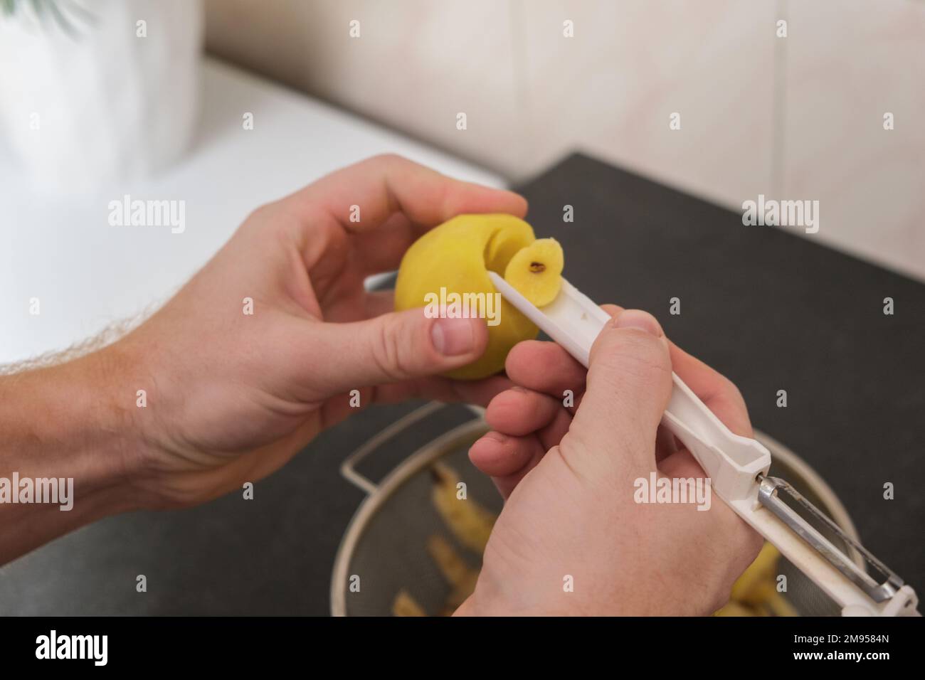 A man peels potatoes with a vegetable peeler, cuts out the lateral bud