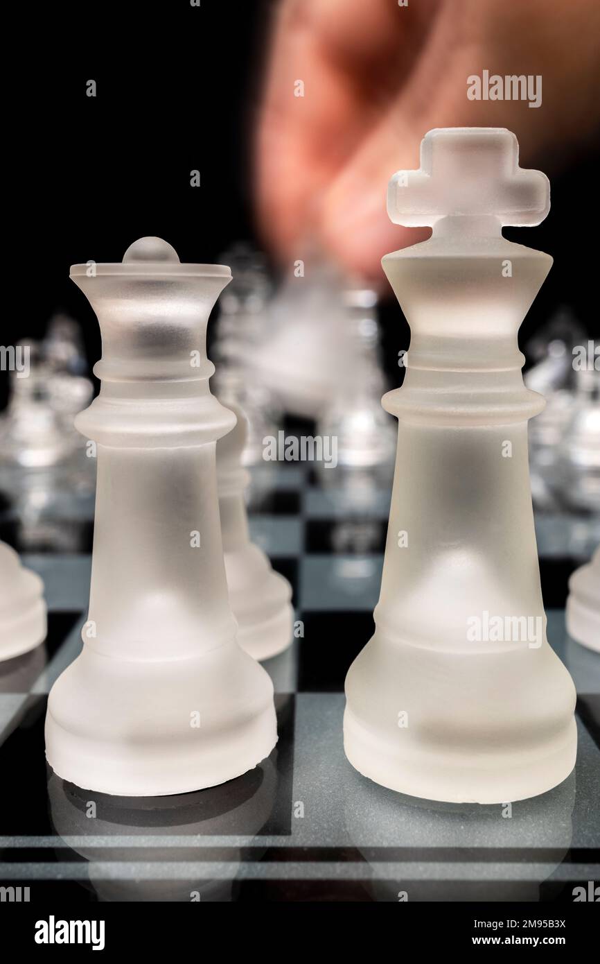 King and queen glass chess pieces with player moving a pawn Stock Photo