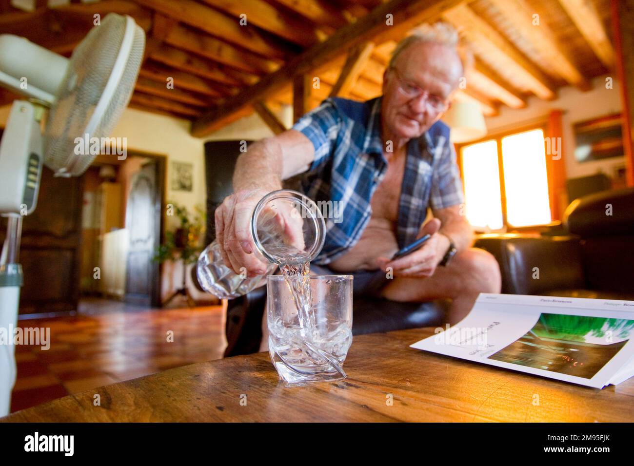 Senior citizens and heat wave: staying hydrated. Intense heat: old man drinking water and fan blowing air. Illustration, elderly people and hydration, Stock Photo