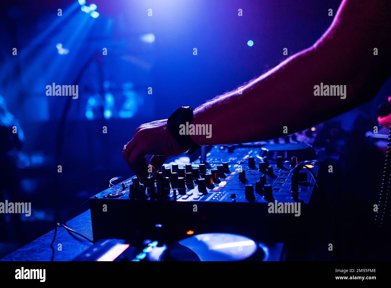 DJ in the night club manages and mixes music on the mixer moving the