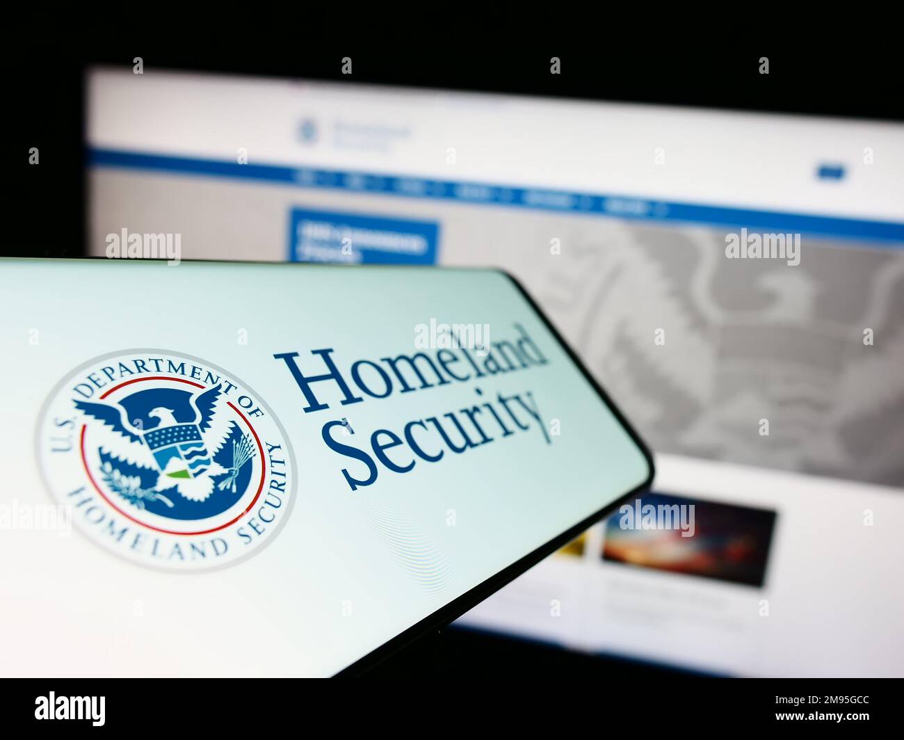 Mobile phone with seal of American Department of Homeland Security (DHS) on screen in front of website. Focus on center-left of phone display. Stock Photo