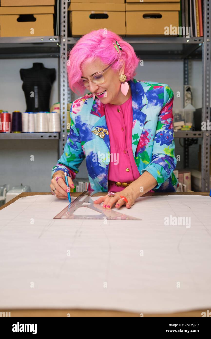 Dressmaker with pink hair and colorfull clothes drawing sewing patterns. Stock Photo