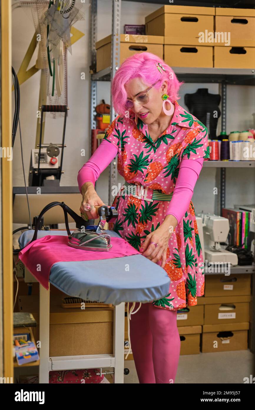 Seamstress with pink hair and colorfull clothes ironing fabric. Stock Photo