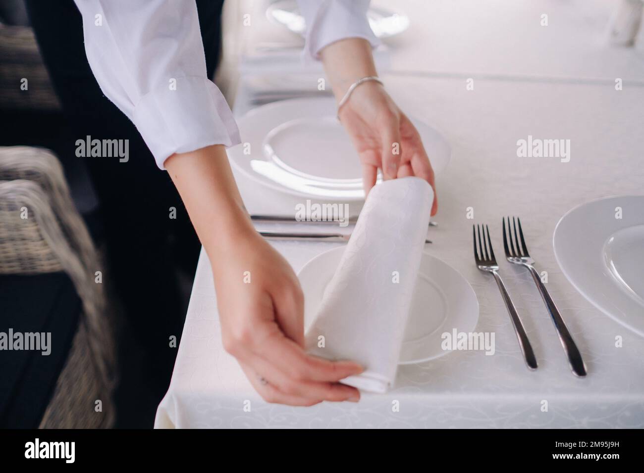The waiter puts a white napkin on the plate. Beautiful table setting for a holiday without food. Stock Photo
