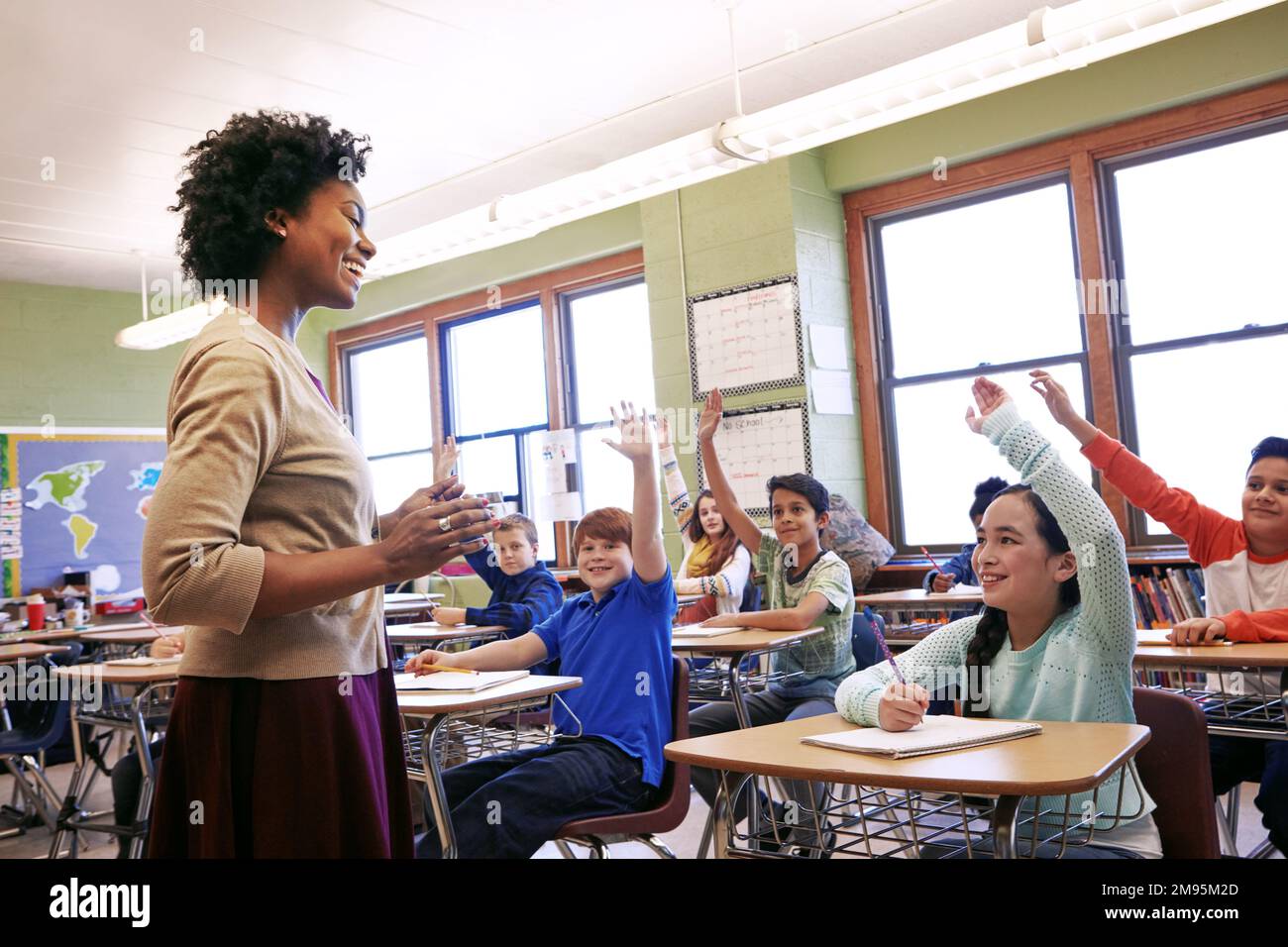 School, teacher and children raise their hands to ask or answer an academic question for learning. Diversity, education and primary school kids Stock Photo