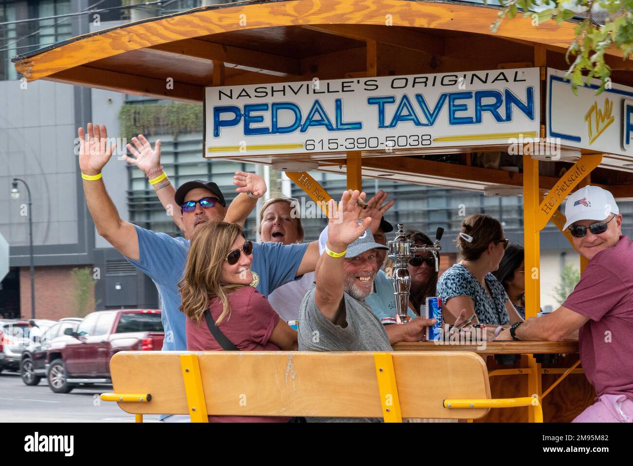 Happy tourists smile and wave while on a Pedal Tavern, a human-powered vehicle, pedaling their mobile pub on a tour of downtown Nashville, Tennessee. Stock Photo