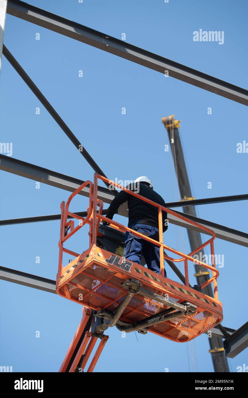 Building site: worker on an aerial work platform installing a metal structure on a building under construction Stock Photo