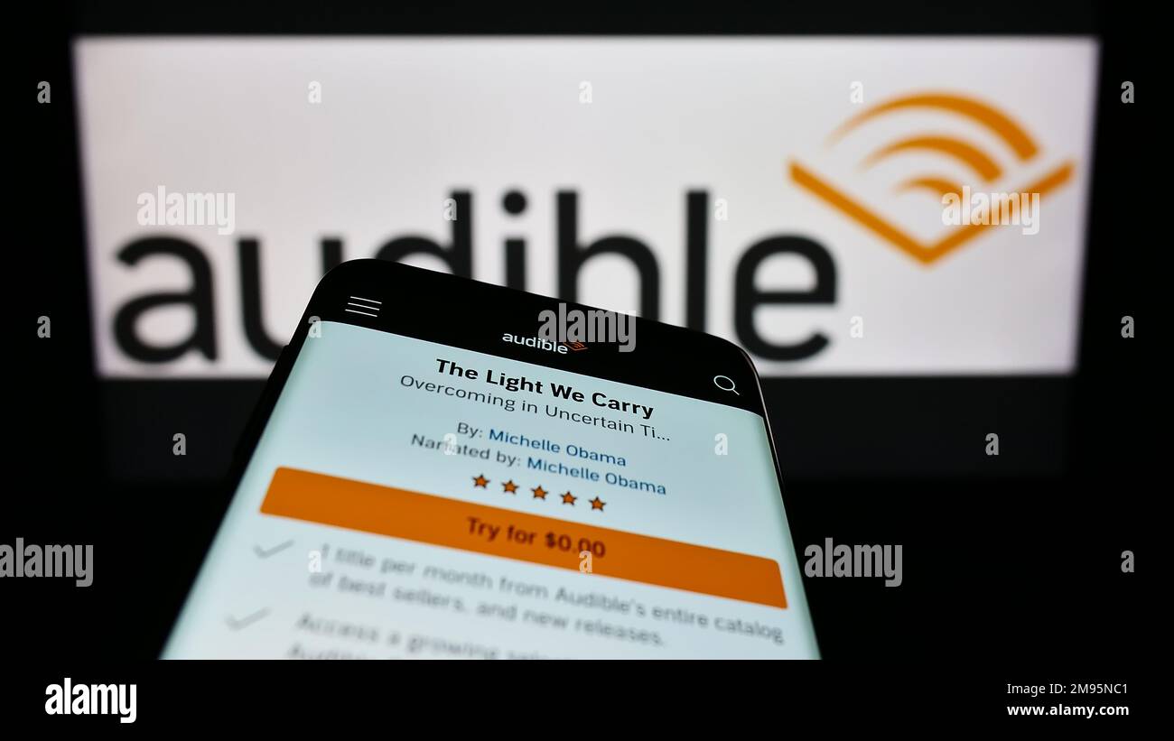 Mobile phone with web page of American audiobook company Audible Inc. on screen in front of business logo. Focus on top-left of phone display. Stock Photo