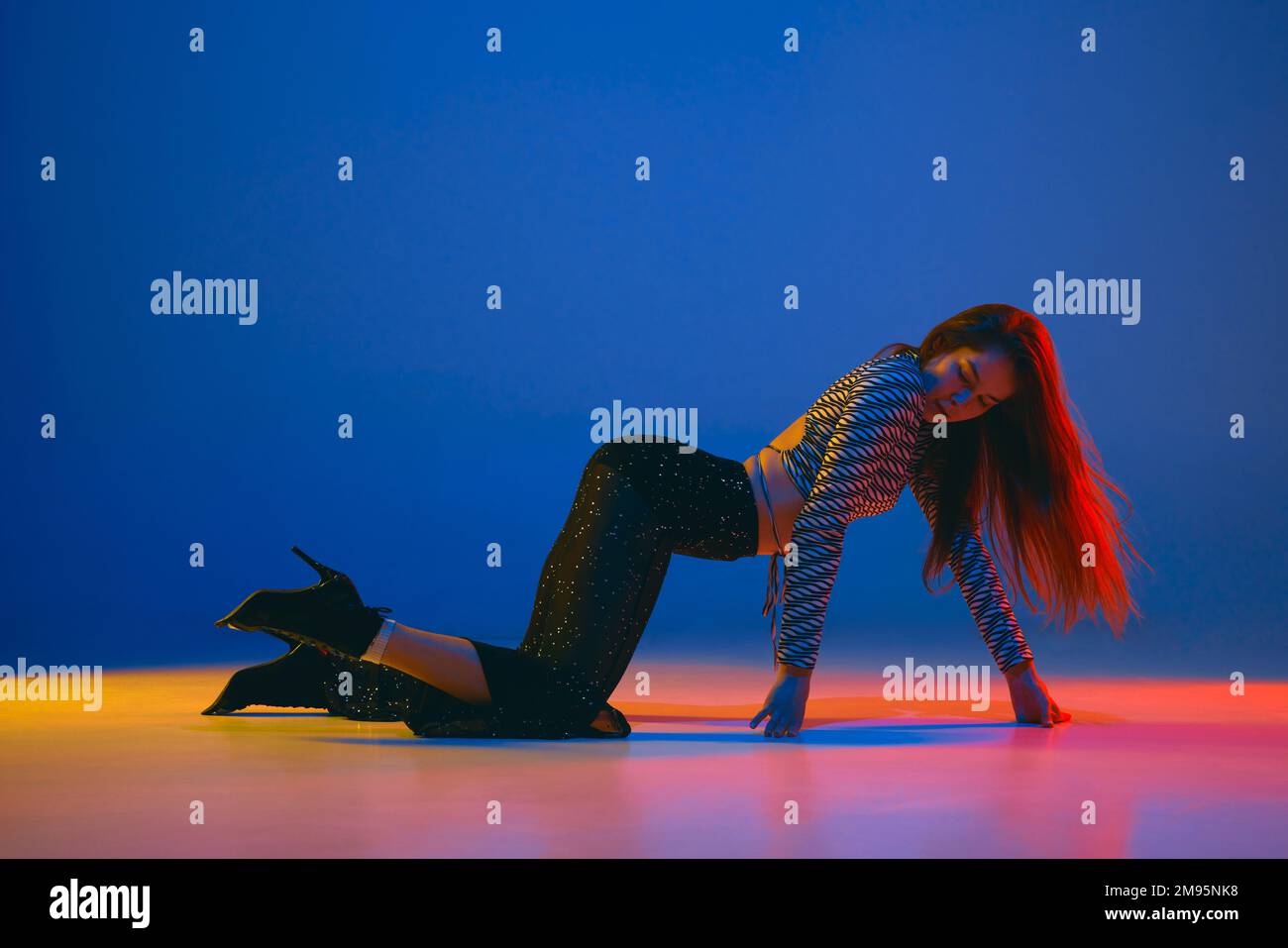 Self-expression. Young girl dancing high heel dance in stylish clothes over blue background in neon light. Concept of modern dance style Stock Photo