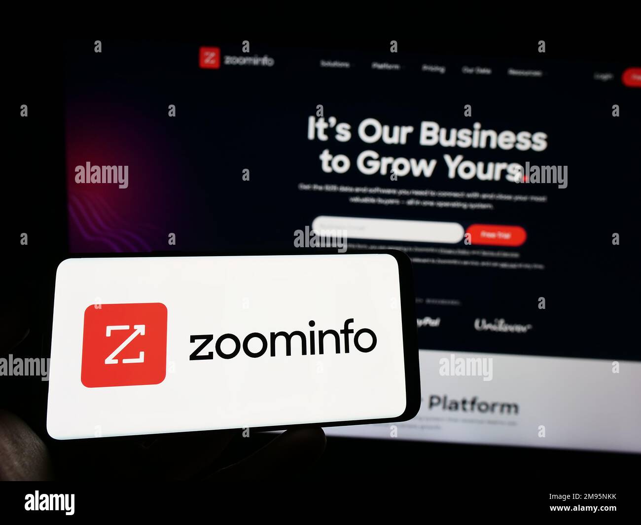 Person holding smartphone with logo of US software company ZoomInfo Technologies Inc. on screen in front of website. Focus on phone display. Stock Photo