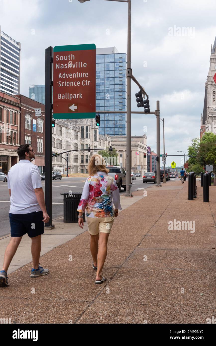 Middle aged couple, man and woman, look up while walking by a sign in Nashville, TN, that reads “South Nashville, Adventure Science Ctr, Ballpark. Stock Photo