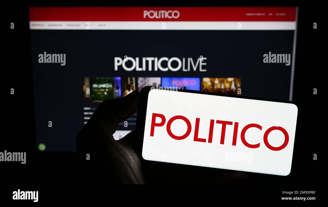 Person holding mobile phone with logo of US political newspaper company Politico LLC on screen in front of web page. Focus on phone display. Stock Photo