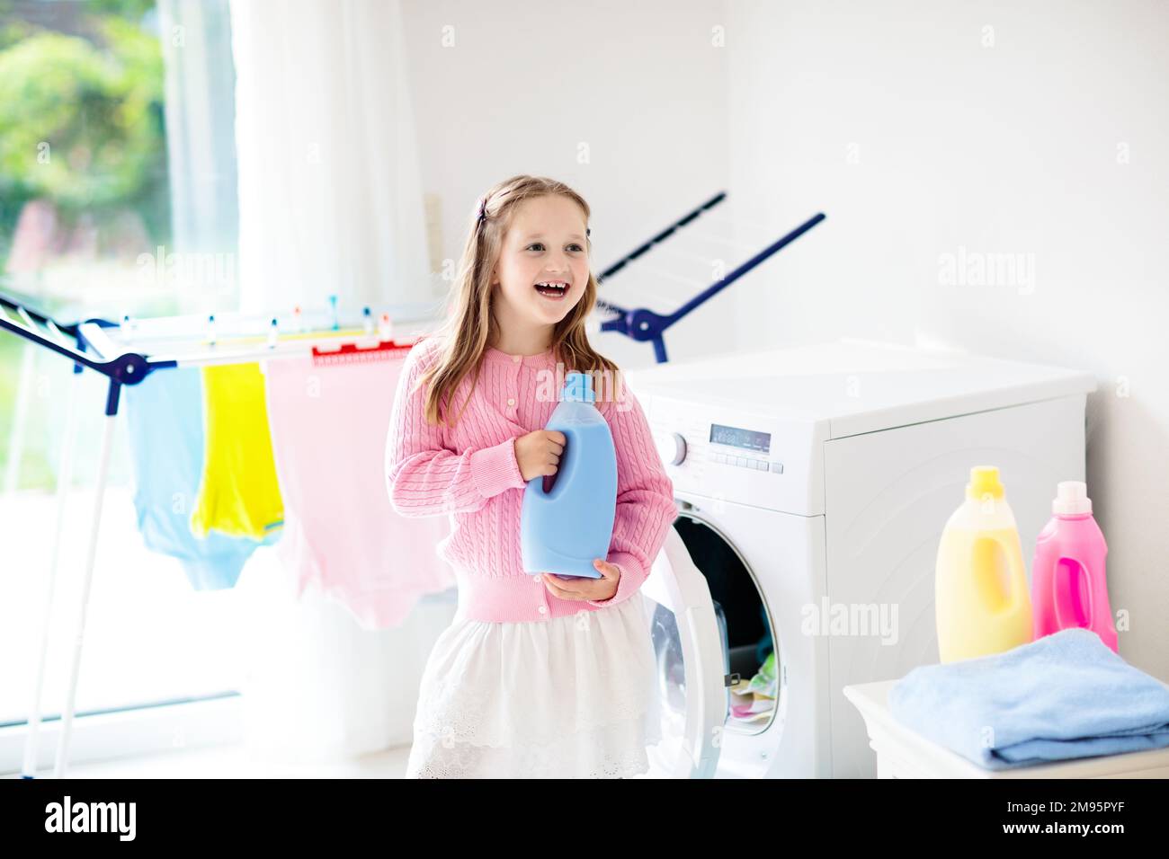Child in laundry room with washing machine or tumble dryer. Kid helping