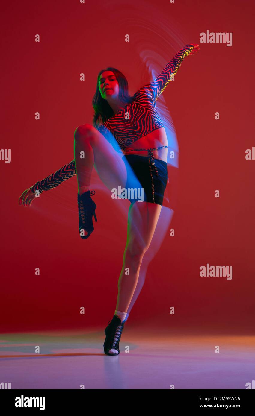 Balancing. Portrait of young girl dancing heels dance over red background in neon with mixed light. Concept of modern dance style Stock Photo