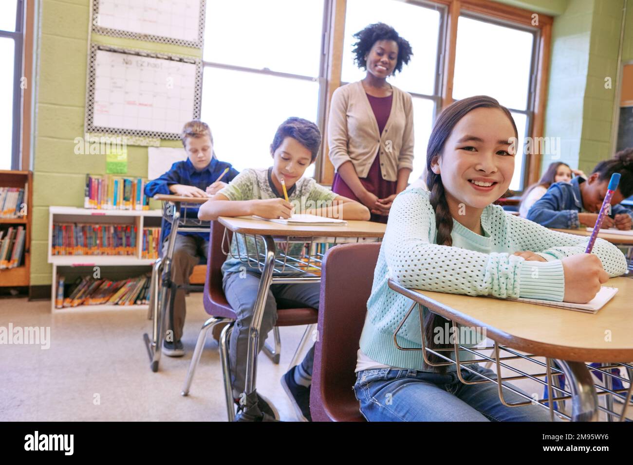 Education, exam and portrait of a girl in class to study, writing and test at school. Happy, learning and student with a smile for studying in a Stock Photo
