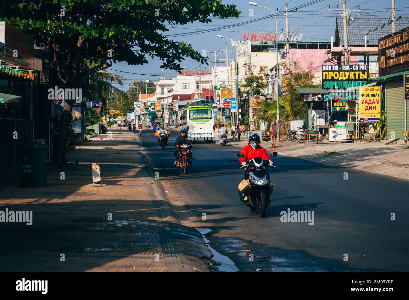 MUI NE, VIETNAM - CIRCA MARCH 2017: A lot of people riding on motorbikes on the road against the background of advertising and shops Stock Photo