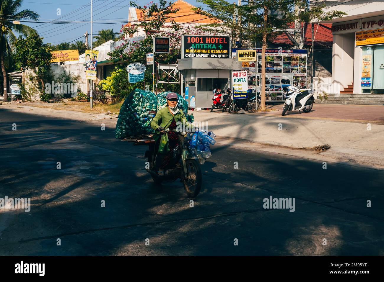 MUI NE, VIETNAM - CIRCA MARCH 2017: Elderly woman riding a motorbike and carries empty bottles of beer and water Stock Photo