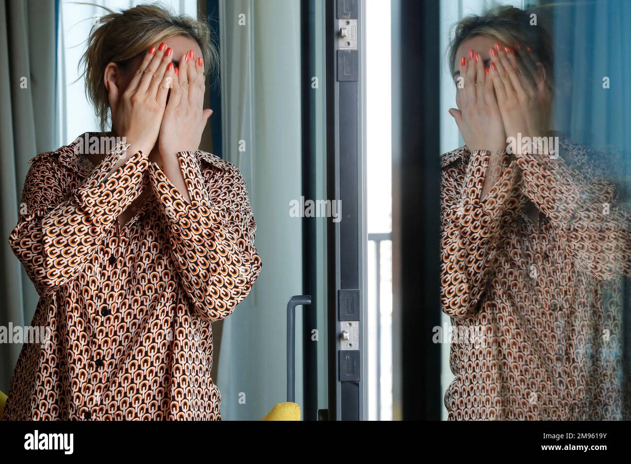 Woman covering her face with her hand. Depression.  Reflection in window. Stock Photo