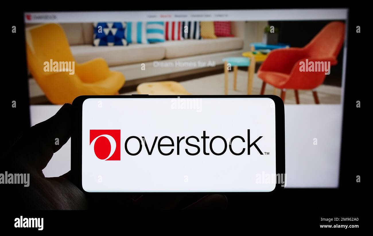 Person holding smartphone with logo of US e-commerce company Overstock.com Inc. on screen in front of website. Focus on phone display. Stock Photo