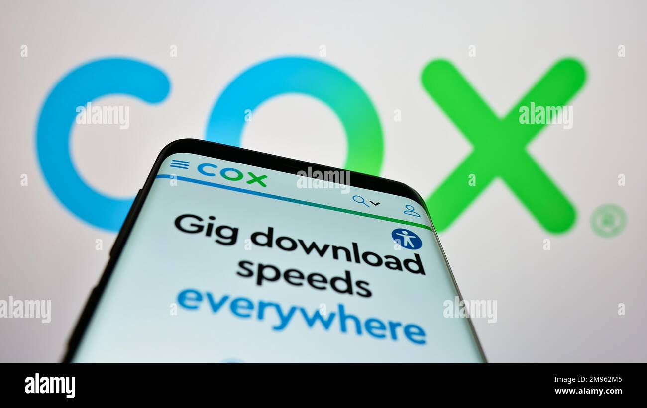 Mobile phone with website of US cable TV company Cox Communications Inc. on screen in front of business logo. Focus on top-left of phone display. Stock Photo