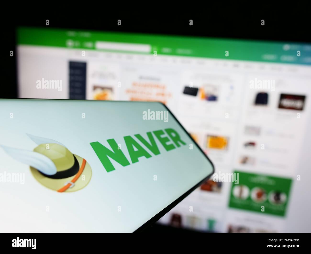 Cellphone with logo of search engine company Naver Corporation on screen in front of business website. Focus on center-left of phone display. Stock Photo