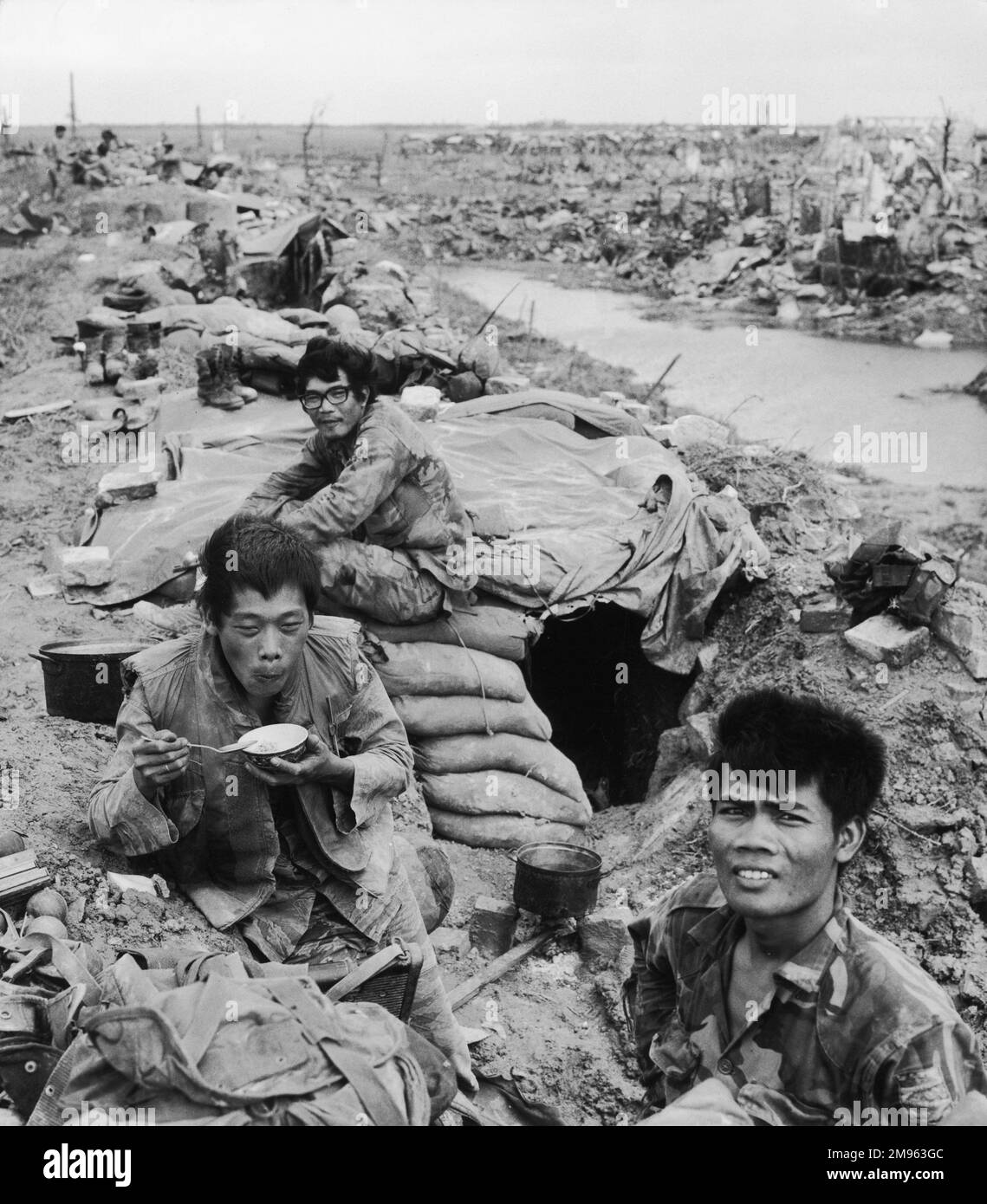 Quang Tri: Three Vietnamese soldiers rest, (one eating rice), among the rubble of their town which has been destroyed by Viet Cong attacks Stock Photo
