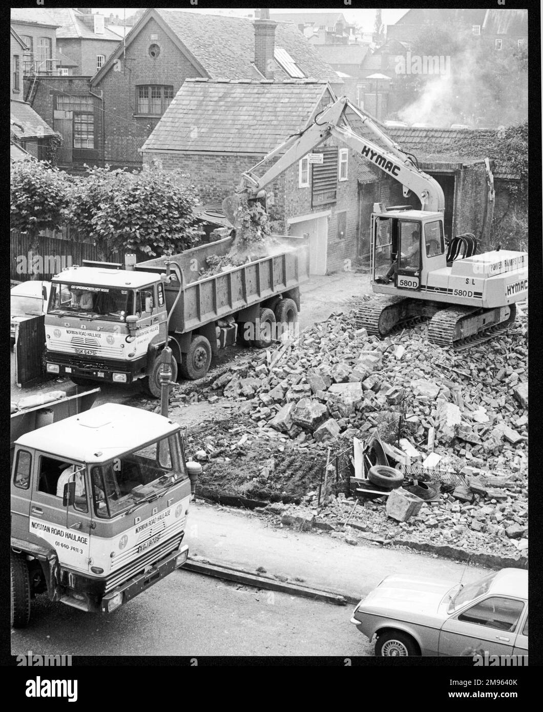 A domestic building site is cleared of rubble and wreckage by a mechanical digger and two haulage trucks Stock Photo