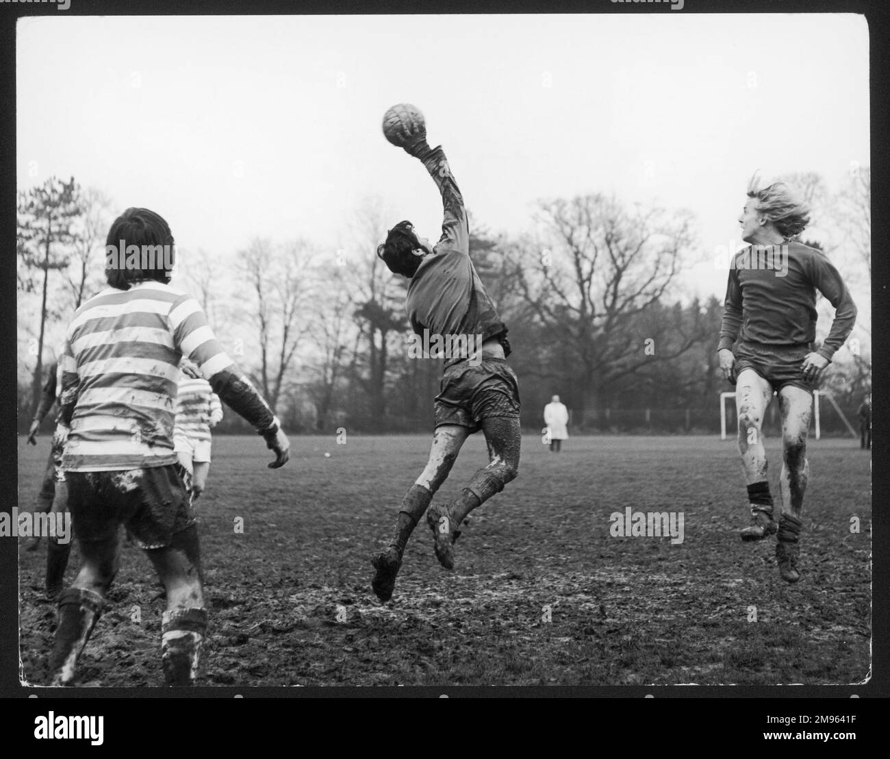 An amateur game of football played on a very muddy pitch: the goalkeeper catches the ball in mid-air Stock Photo