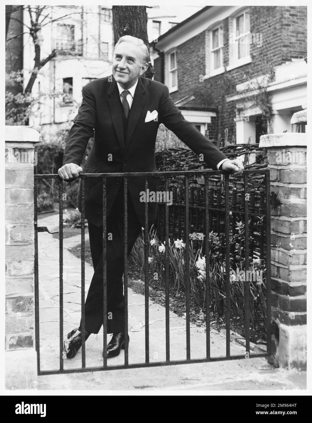 A mature man in a three piece suit poses behind a garden gate. Stock Photo