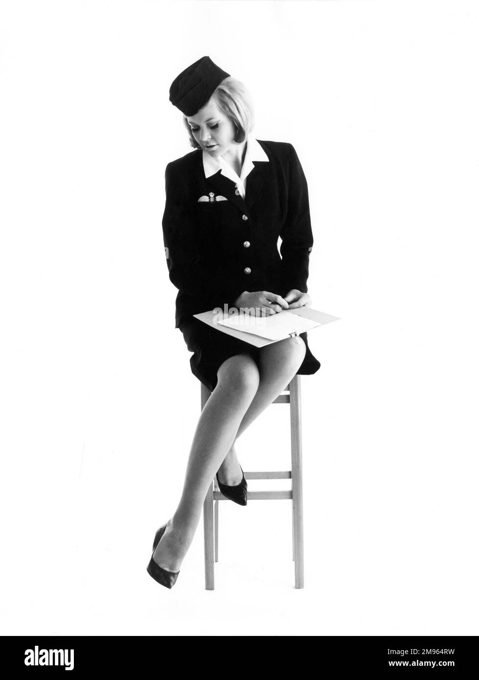 An air hostess sits on a stool with a clipboard on her lap. Stock Photo