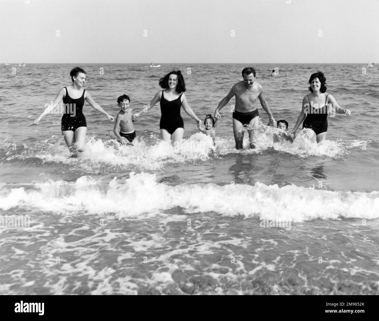 A family all hold hands as they run out of the sea. Stock Photo