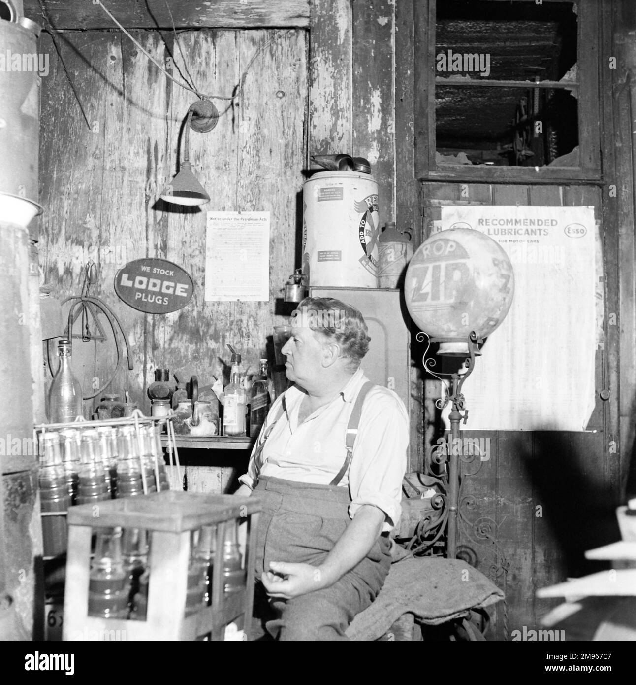Worcestershire garage and seated owner surrounded by oils, engine treatments and lubricants. Photograph by Norman Synge Waller Budd Stock Photo
