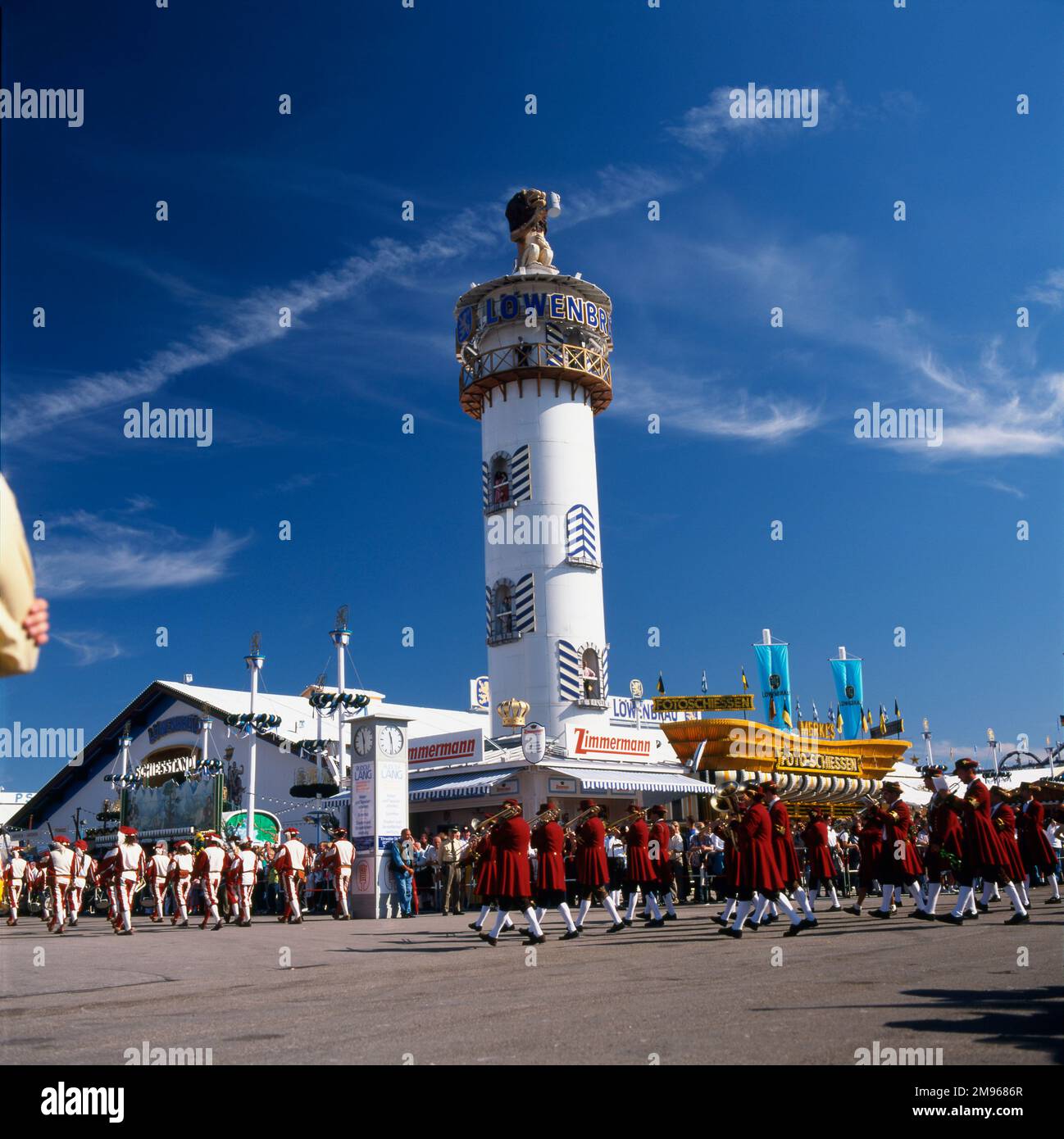 Scene at the Oktoberfest in Munich, Germany, with a marching band in folk costumes making their way past the tower of the Lowenbrau Brewery. Stock Photo