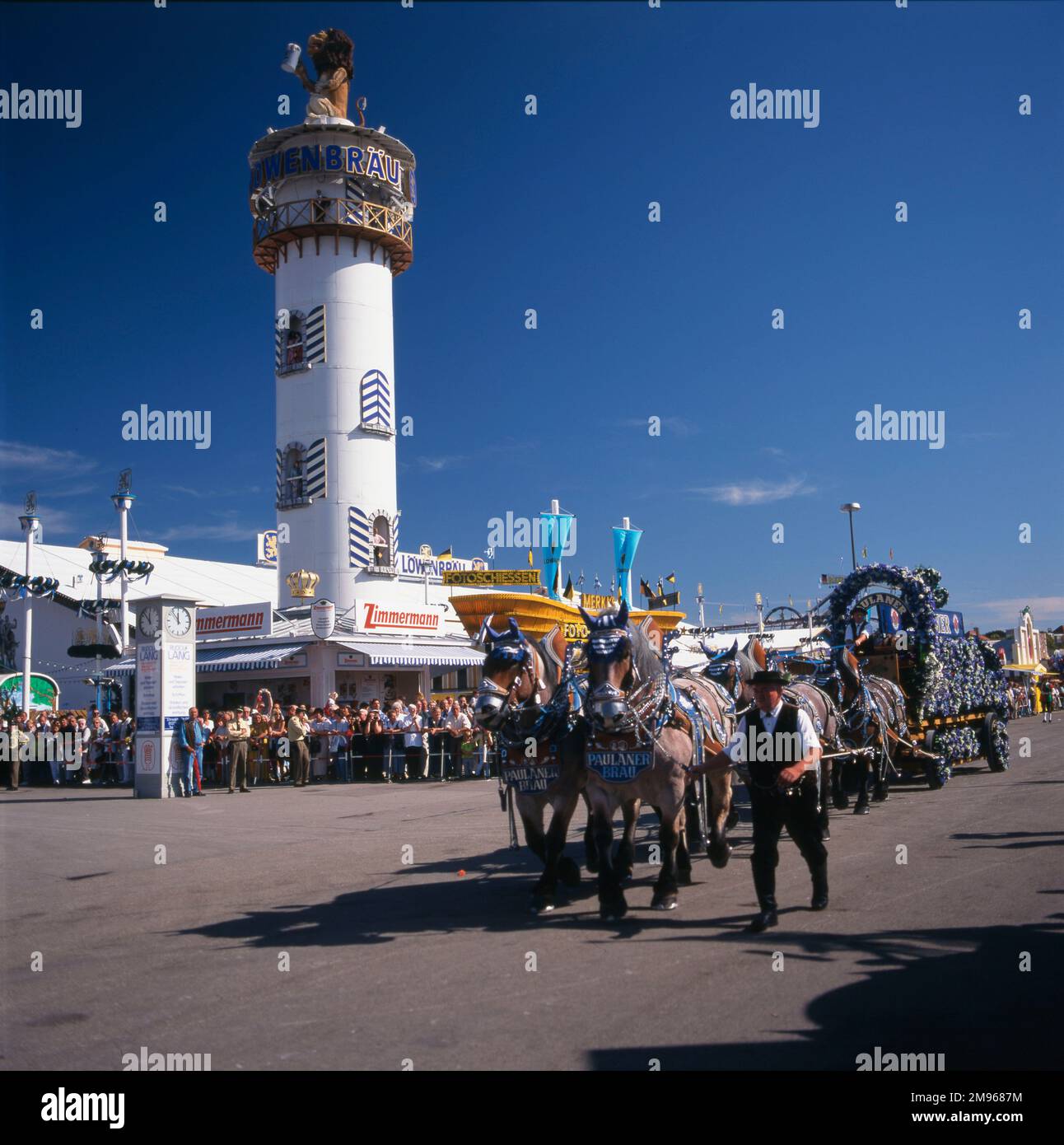 Scene at the Oktoberfest in Munich, Germany, with horses pulling a decorated dray past the tower of the Lowenbrau Brewery. Stock Photo