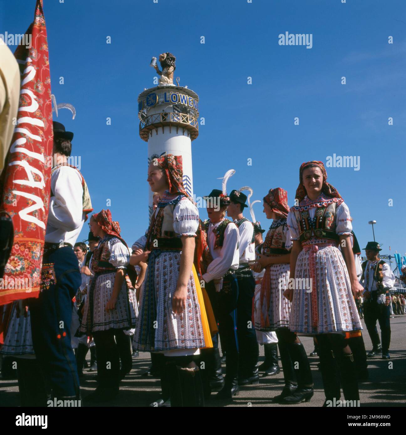 Scene at the Oktoberfest in Munich, Germany, with people in folk costume and the tower of the Lowenbrau Brewery in the background. Stock Photo