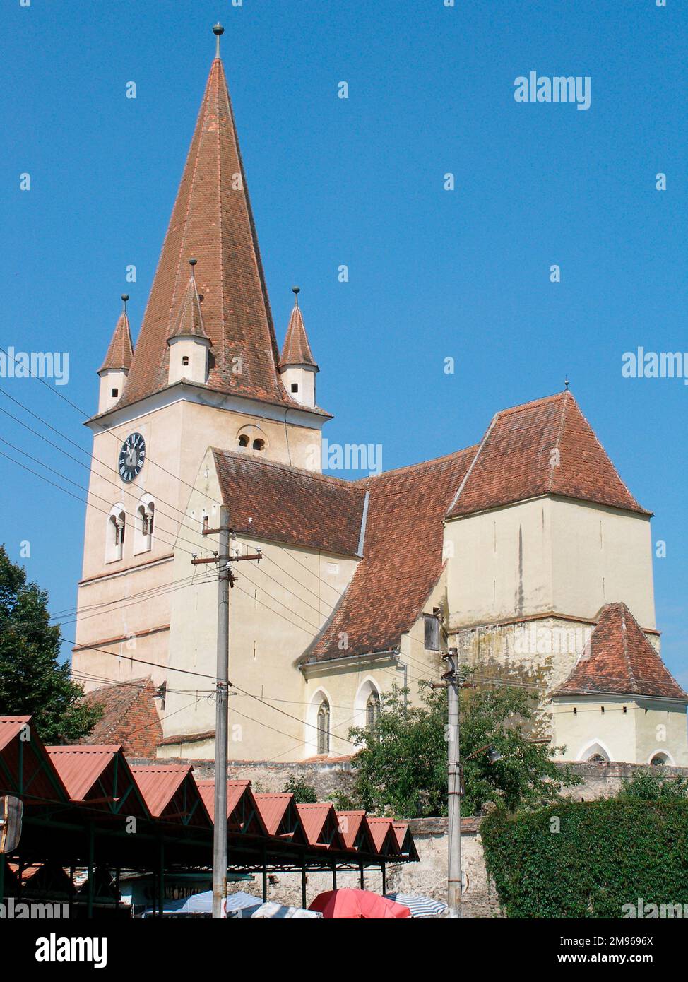 View of a medieval fortified church in Cisnadie (Heltau), Sibiu, in Transylvania, Romania, with a street market just visible below.  The church was built in the 12th century and fortified in the 15th. Stock Photo