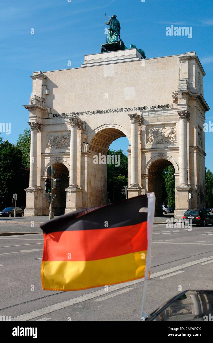 View of a waving German flag in front of the triple-arched Siegestor (Victory Gate or Triumphal Arch) in Munich, Bavaria, Germany.  The gate was completed in 1852, and dedicated to the Bavarian Army.  After heavy damage during the Second World War it was restored, and is now a monument to peace. Stock Photo