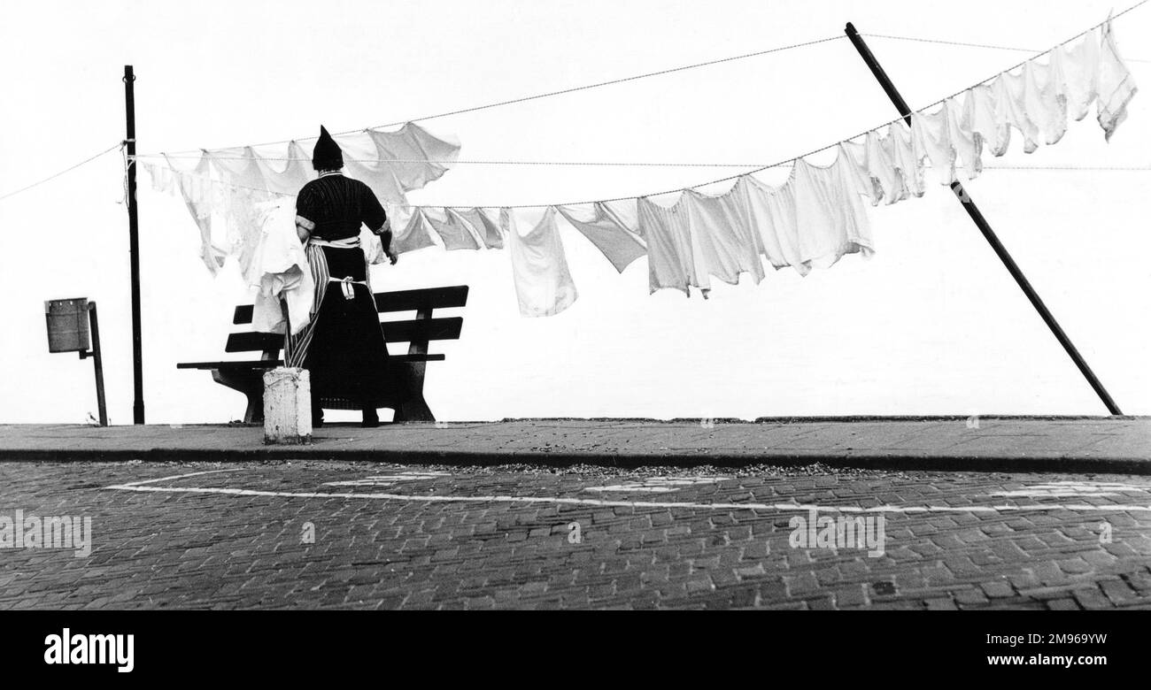 A woman hanging out the washing on a line (or two), apparently at the side of a stretch of water. Stock Photo