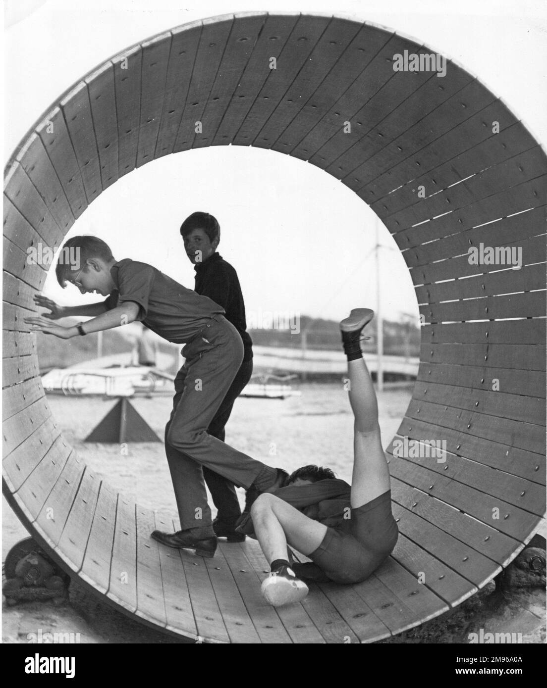 Three boys playing inside a large barrel.  One of them has lost his footing and has fallen over. Stock Photo