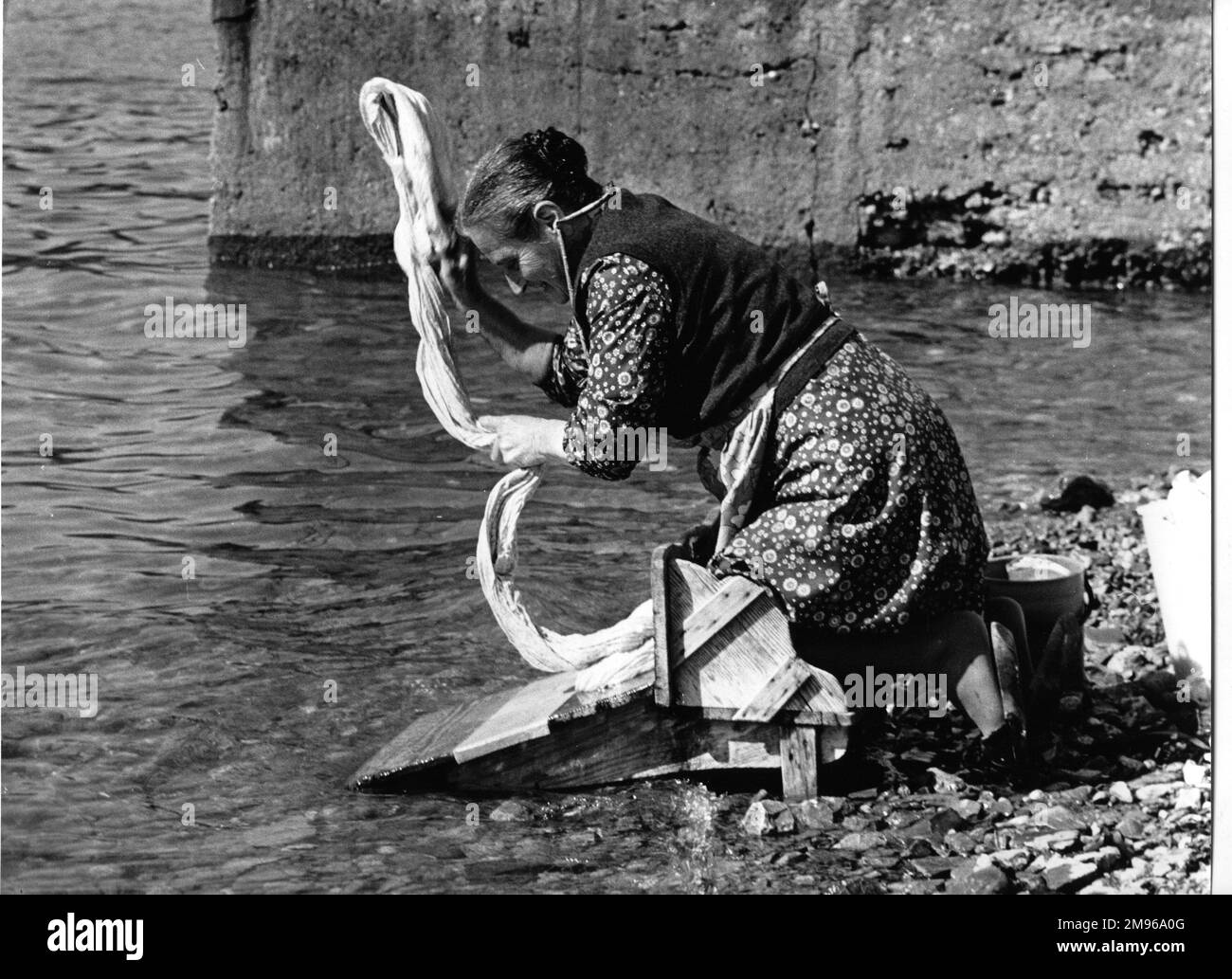 Woman washing a sheet at the side of a river in Portugal.  She is kneeling on a specially designed wooden platform, which stops her getting too wet. Stock Photo