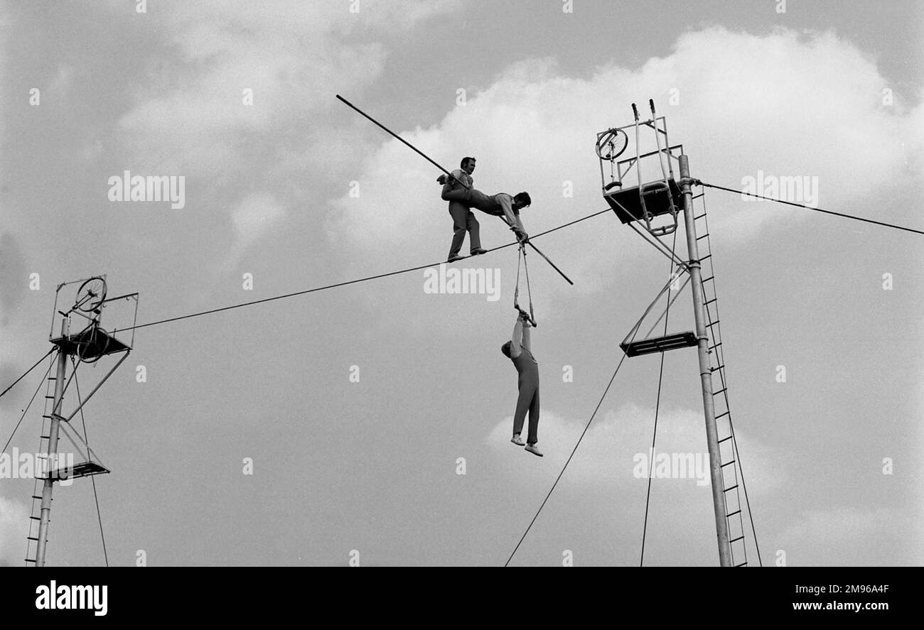 Three acrobats doing a balancing act on a high wire in the open air. Stock Photo