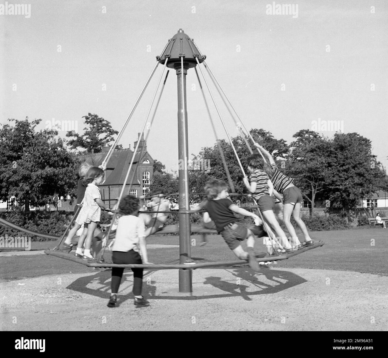 A group of children playing on an umbrella style roundabout on Lindfield Common, Sussex, England. Stock Photo