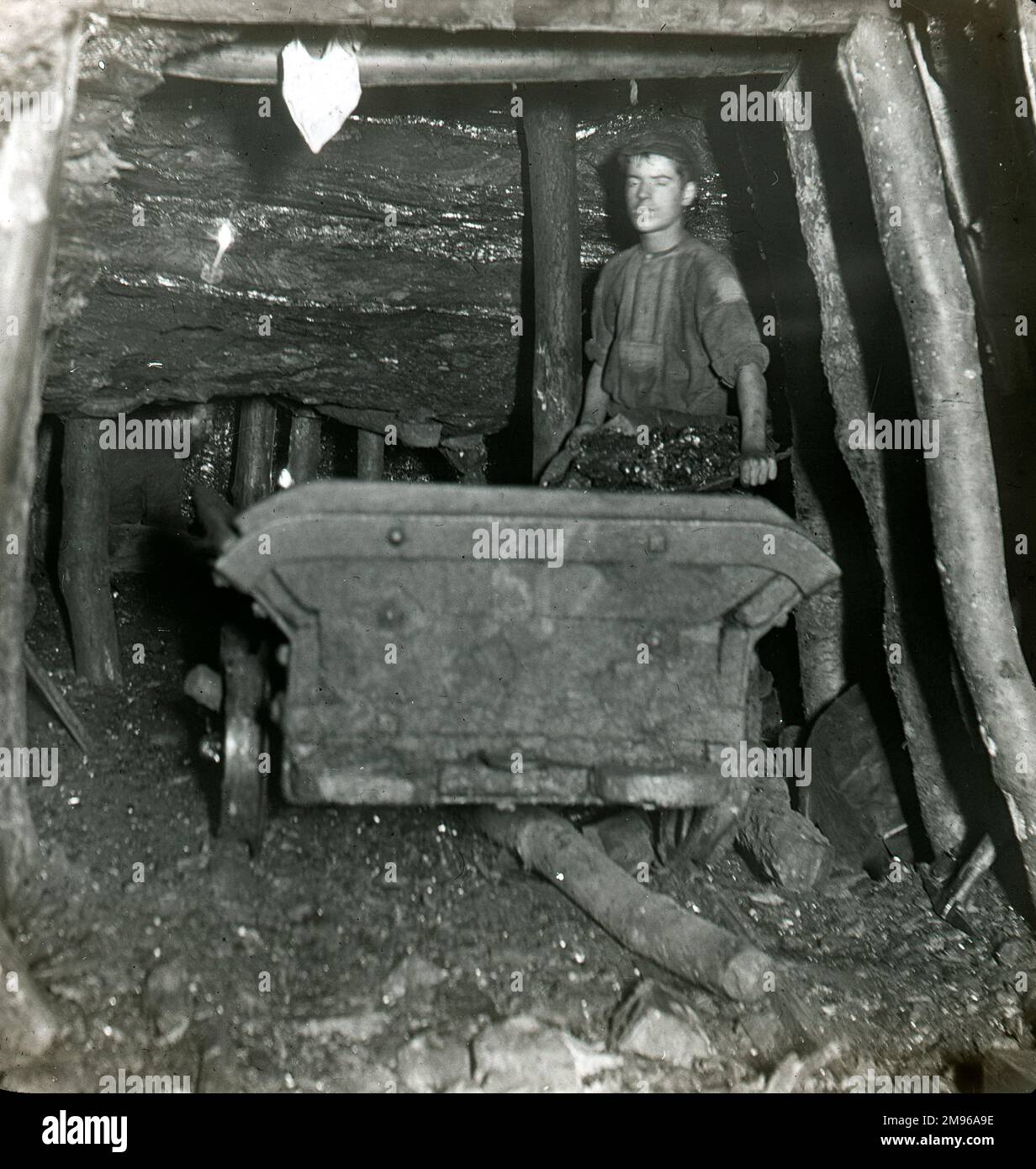 A coal miner (Billy Hurland) filling a dram (coal truck) at Baldwin's Level (nicknamed Clog and Legging) in a coalmine near Pontypool in South Wales.  Another collier can be seen, centre left, in a narrow coal seam. Stock Photo