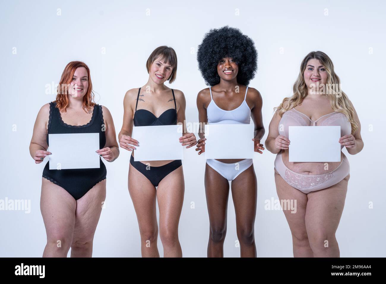 Multiracial group of women holding blank white board over belly, body positive concept, copy space on empty signs to write what you want Stock Photo