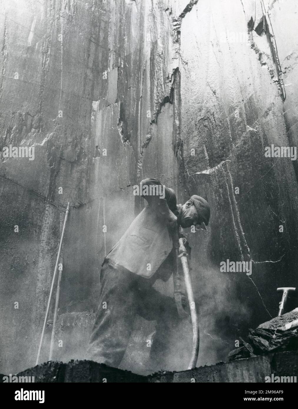 A quarryman drilling into the rock at Penyrorsedd Slate Quarry, Nantlle Valley, Caernarvonshire (now Gwynedd), North Wales. The silica dust in the air is lethal, giving rise to silicosis, an incurable respiratory disease affecting most slate quarry workers in middle age. Stock Photo