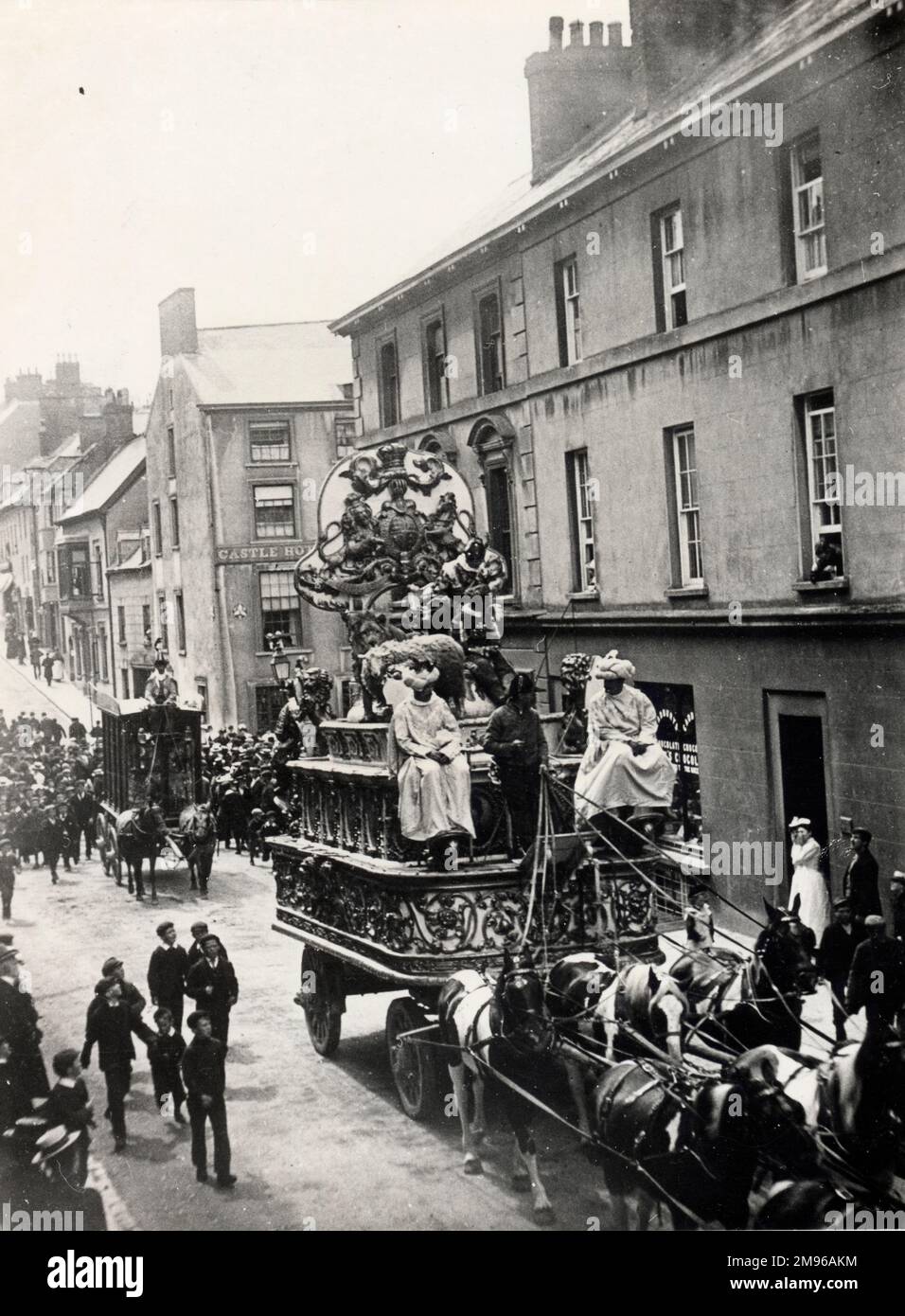 Street scene, showing Sanger's Circus visiting Haverfordwest, Pembrokeshire, Dyfed, South Wales.  There are two elaborate horse-drawn carriages, with riders dressed in fancy costumes.  An excited group of schoolboys are following the first carriage along the road.  Sanger was a famous circus impresario, staging spectacular shows at large venues all over the country from the 1850s onwards. Stock Photo