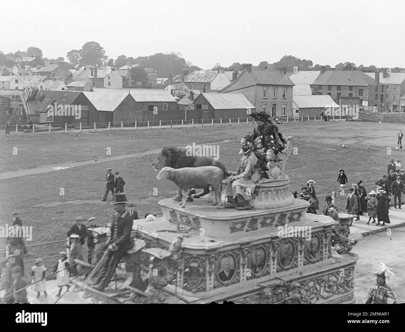 Street scene, showing part of Sanger's Circus parade during a visit to Haverfordwest, Pembrokeshire, Dyfed, South Wales.  This elaborate horse-drawn carriage includes a lion and a lamb, with riders dressed in fancy costumes.  People on the pavements stop and look.  Sanger was a famous circus impresario, staging spectacular shows at large venues all over the country from the 1850s onwards. Stock Photo