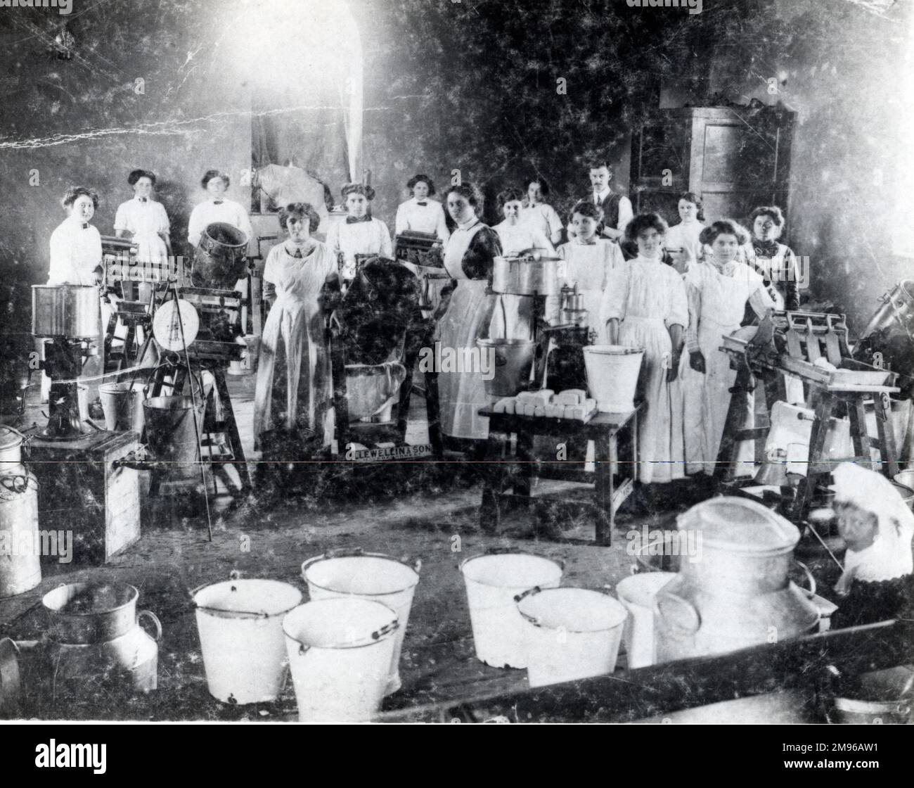 A group of employees, mostly women, of the Llewellin Churn Works at North Gate, Haverfordwest, Pembrokeshire, Dyfed, South Wales.  Butter making equipment can be seen, as well as fresh pats of butter, large milk churns, and enamelled buckets for moving milk. Stock Photo