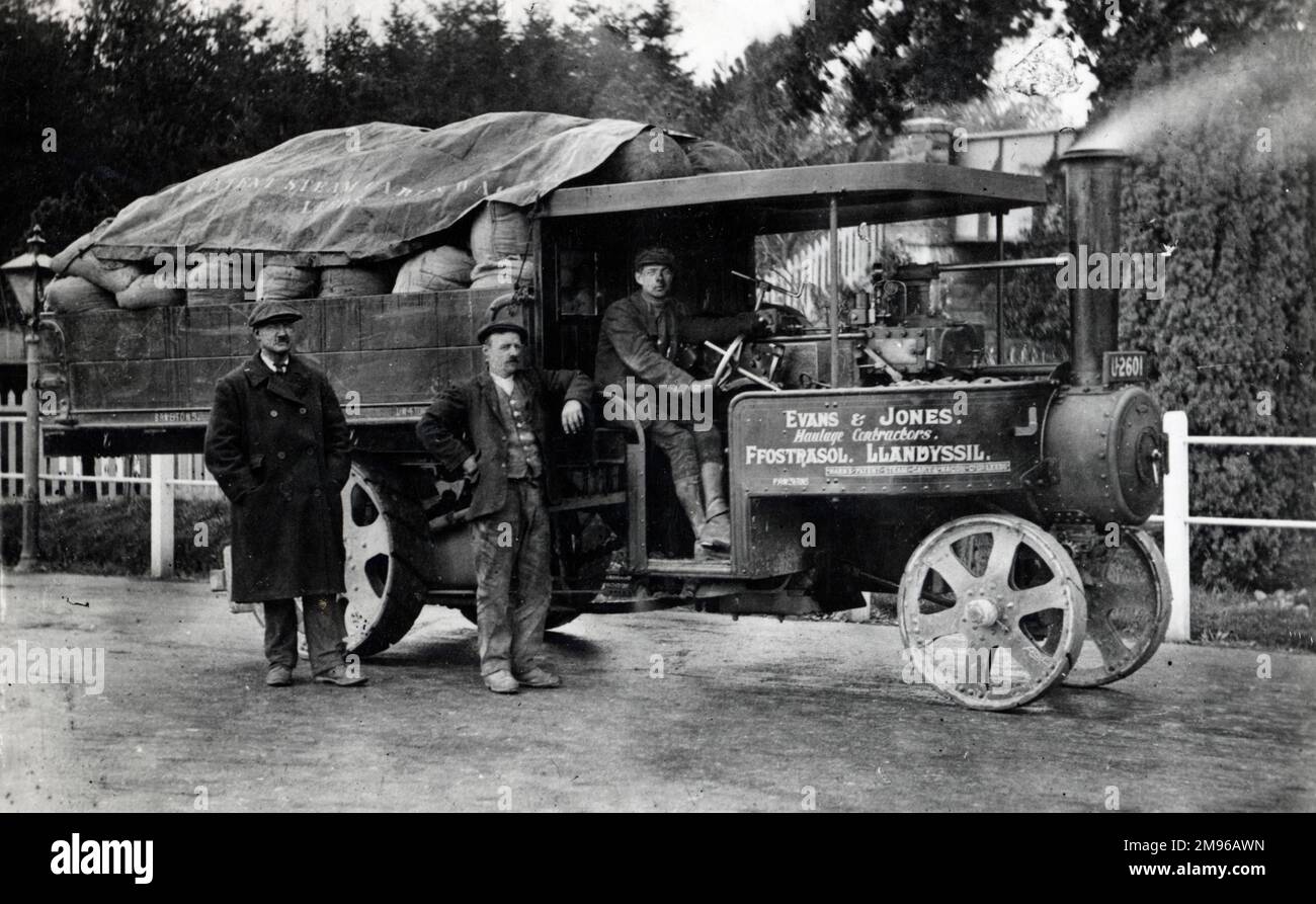 A steam lorry (Mann's patent steam cart) belonging to Evans & Jones, haulage contractors, laden with goods which have just been loaded from a train at Llandysul (or Llandyssil) railway station in Powys, Mid Wales.  The driver sits at the wheel, and two men stand at the side. Stock Photo