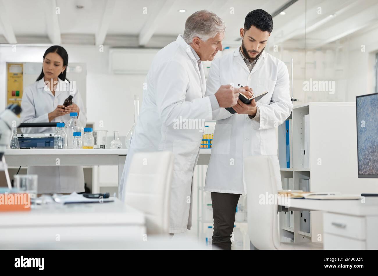 Always keep a detailed data record of every experiment. two scientists writing notes while having a discussion in a lab. Stock Photo